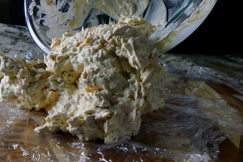 transferring the ingredients for jalapeno popper cheese ball to plastic wrap