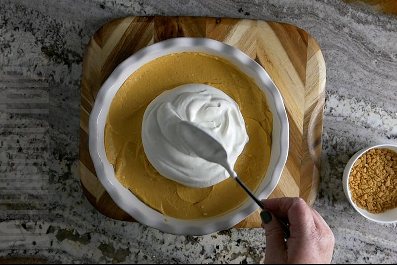 adding homemade whipped cream to the top of the pumpkin cheesecake dip